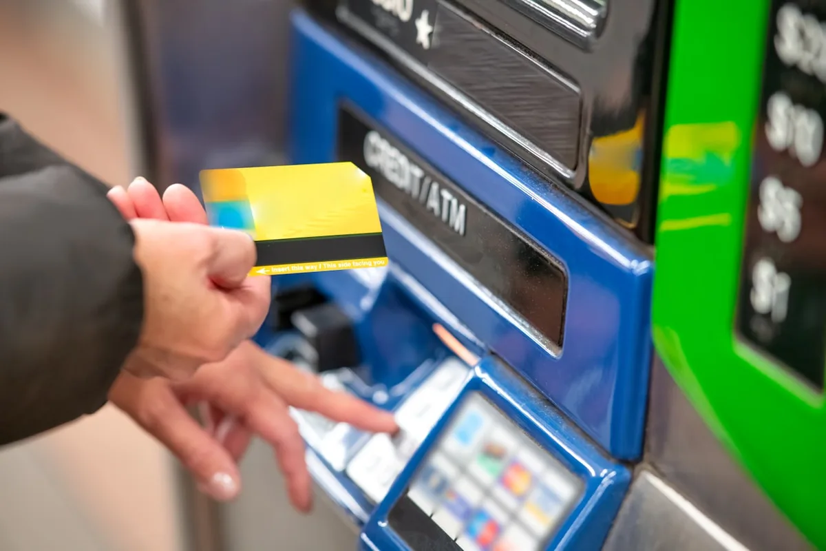 파란색 CREDIT/ATM 기기에 카드를 넣으려는 손을 가까이 찍은 사진으로, 해외 ATM 출금과 카드 결제 때 붙는 숨은 수수료를 점검해야 함을 나타낸다